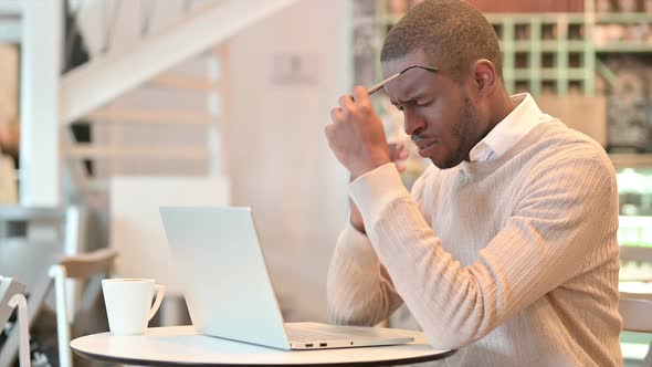 Stressed African Man with Laptop Having Headache in Cafe