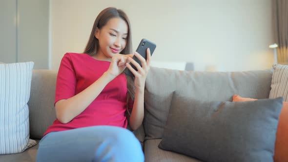 Happy Asian Female Texting on Mobile Phone While Sitting on Sofa in Family Home. Static Full Frame,