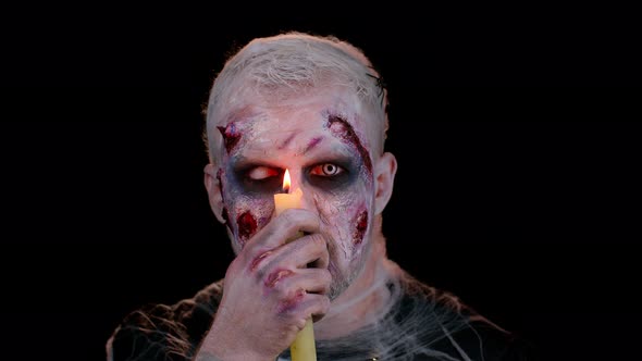Man with Halloween Zombie Bloody Wounded Makeup Trying to Scare Spells Conjures Over a Candle