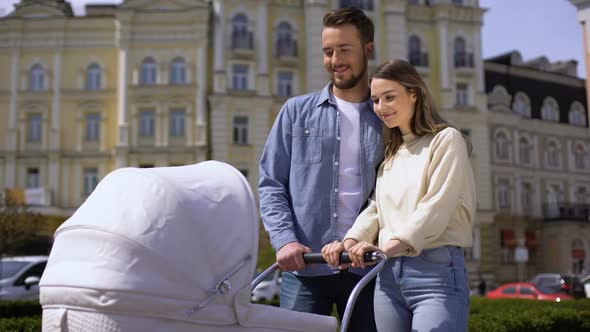 Young Man and Woman Looking at Baby Swinging Carriage, Family Love, Hugging