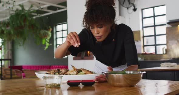 Mixed race female chef preparing a dish and smiling in a kitchen