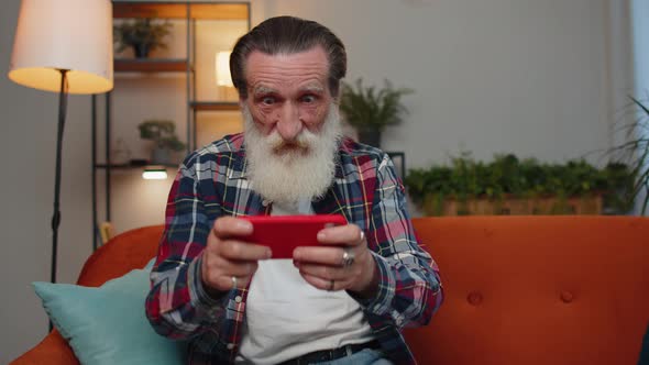 Worried Funny Senior Old Grandfather Man Playing Racing Online Video Games on Smartphone at Home