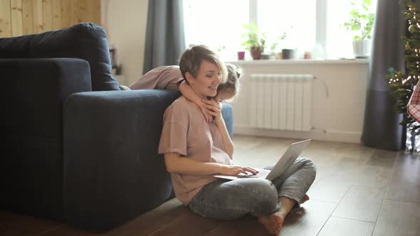 Mom Works on Laptop with Her Daughter Cuddling Her in Living Room Distant Job