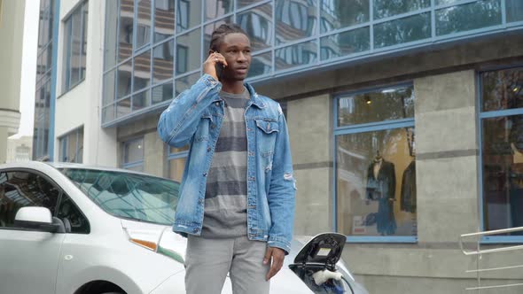 African American Man Talking Phone While Charging Electric Car