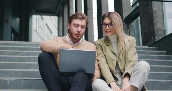 Woman and Man sitting on the Stairs Outdoors Looking in Laptop Successful Win.