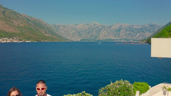 Aerial View a Couple Stands on the Shore of the Bay of Kotor Overlooking the Blue Sea and Mountains