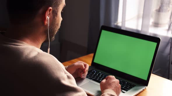 Young Caucasian Man at Home Office Sits Table Communicates Talk Speak with Green Screen Laptop