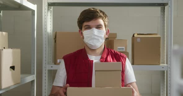 Man Wearing Red Vest Holding Parcels Employee of Warehouse in Medical Face Mask Holds Delivery Boxes