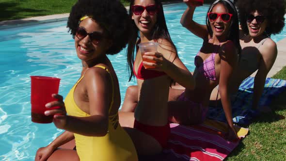 Portrait of group of diverse girls holding drinks while sitting by the pool