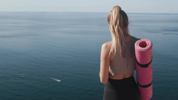 Backside View of Athlete Girl Looking at Phone in Her Hands, Ocean on Background