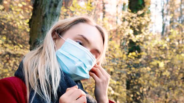 Portrait of a young beautiful woman putting on Corona safety mask amidst orange brown autumn forest