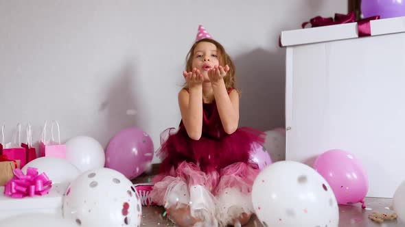 Beautiful little girl blows up multicolored confetti, having fun at home birthday party