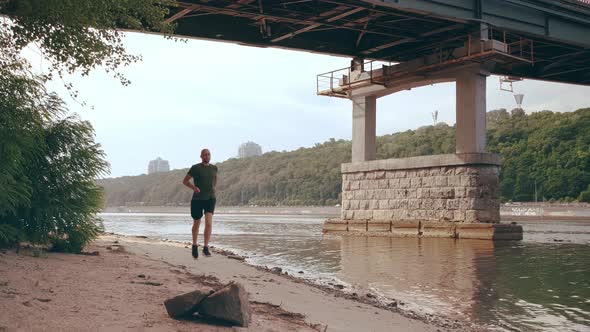 Muscular Young Man Running Under the Bridge on a Sunny Day