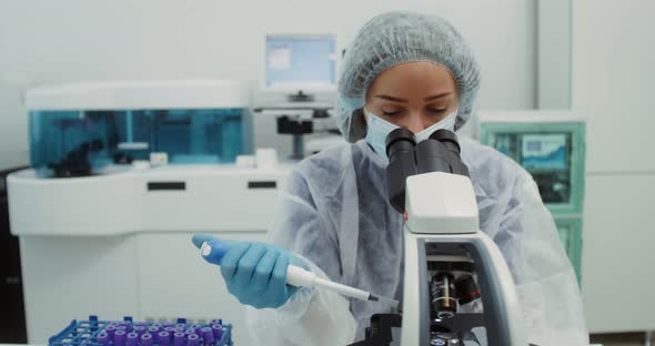 A Scientist in Sterile Clothing Looks Through a Microscope alt