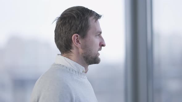 Side View of Anxious Thoughtful Caucasian Man Looking Out the Window in Office