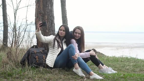 Girls traveling and filming selfie on camera phone. Camping on a cliff in forest