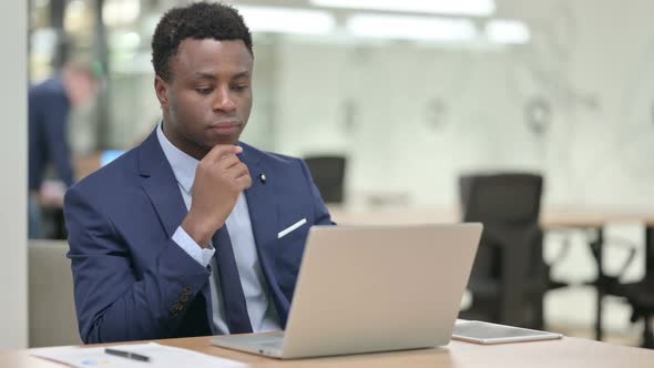 African Businessman Thinking While Using Laptop in Office