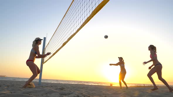 Women players play beach volleyball and a player hitting spiking the ball.