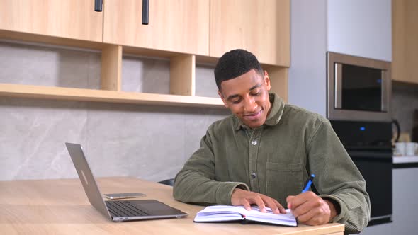 Smiling Multiracial Guy Takes Notes Watching Webinars on the Laptop Researching Business Tasks