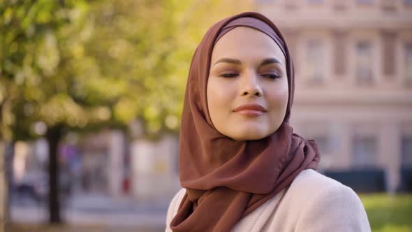 A Young Beautiful Muslim Woman Looks Around with a Smile in a Street in an Urban Area  Closeup