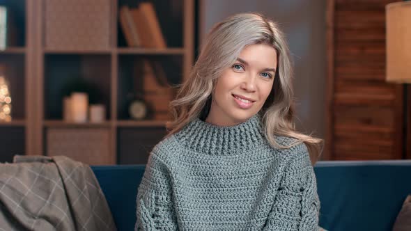 Pretty Blonde Female Wearing Warm Sweater Relaxing on Couch at Comfortable Evening Living Room