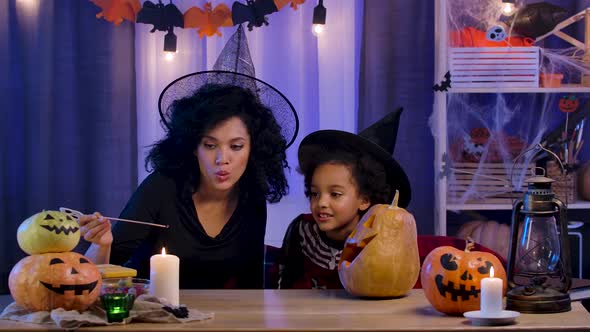 Little Girl and Woman African American in Witch Hat Light Candle in Pumpkin with Carved Smiling Face