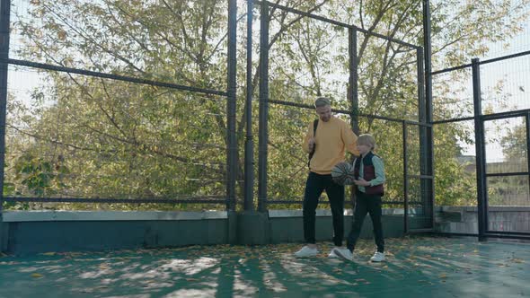 Father with Son Walk Talking on the Basketball Court Boy Runs with a Ball