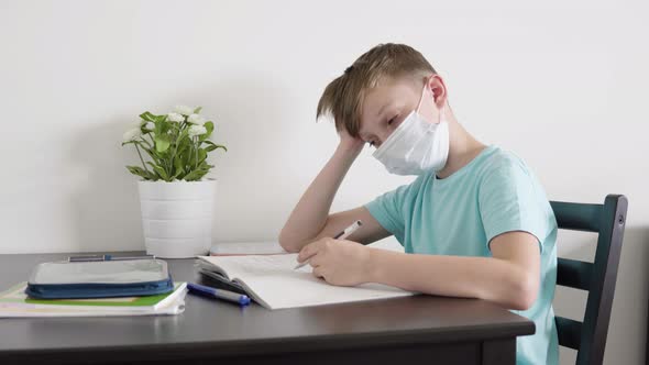 A Young Boy in a Face Mask Falls Asleep As He Does Homework for School at a Table at Home