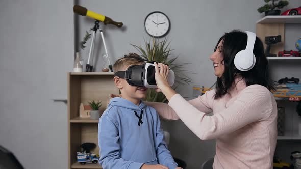 Mother in Earphones Helping Her Joyful Son Putting on the Virtual 3d Glasses at Home