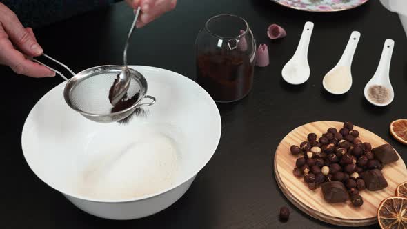 Woman is adding ingredients to flour for making dough for chocolate cake