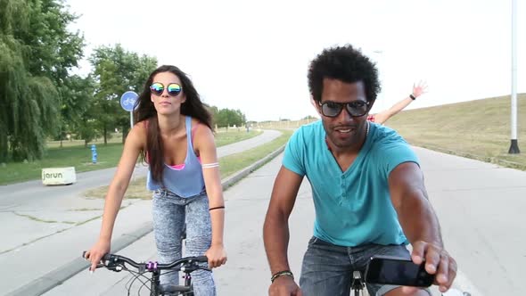 Three young adults having fun cycling and taking selfies