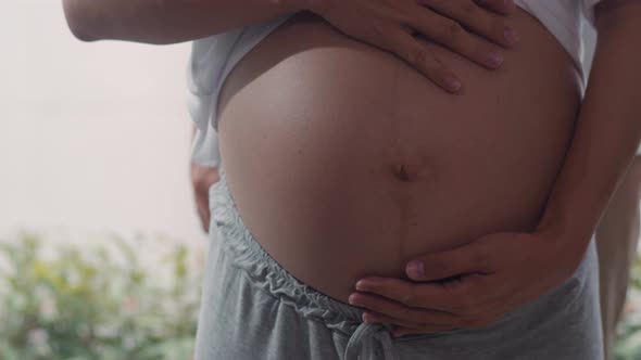 Young Asian Pregnant couple hug and holding belly talking with their child feeling happy smiling