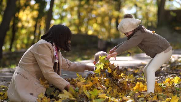 Happy Mom with Special Girl Throwing Leaves on Boy