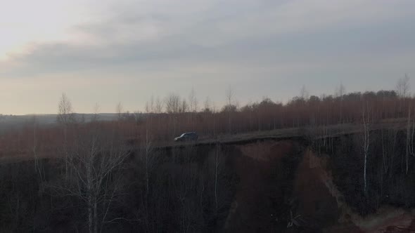 Off road car driving along cliff edge on background yellow field and bare autumn trees aerial view