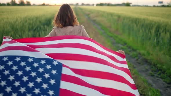 Young Happy Smiling Girl Running with USA Flag Over Wheat Field and Turns Around