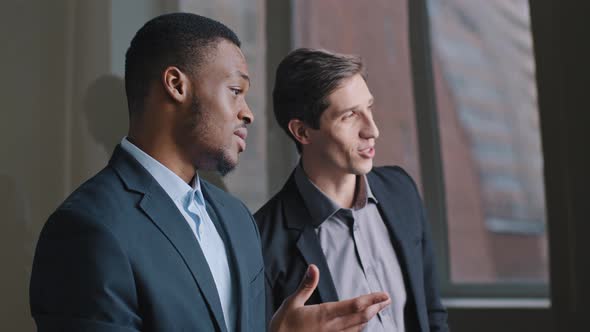 Two Serious Young Businessmen Multiracial Colleagues Standing in Office Looking Out Window Caucasian