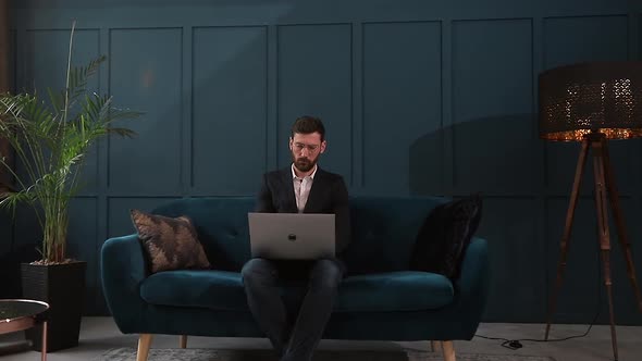 Portrait of an Elegant Businessman Sitting with Laptop on the Couch at the Luxury Blue Office