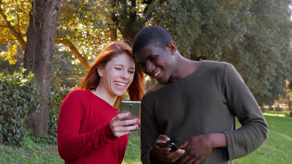 Happy carefree mixed lovers using their smartphones in the park