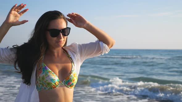 Beautiful Brunette in Sunglasses Running Along Ocean Coast Enjoying Freedom. Portrait of Attractive