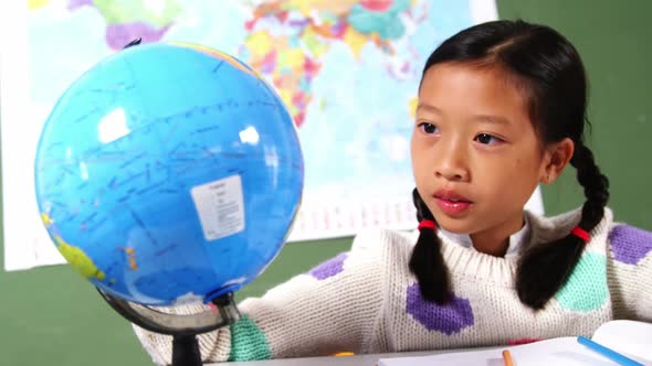 Schoolgirl looking at globe in classroom at school