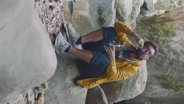 Vertical Shot of Man Traveler Brushing Teeth Sitting Near Mountain River