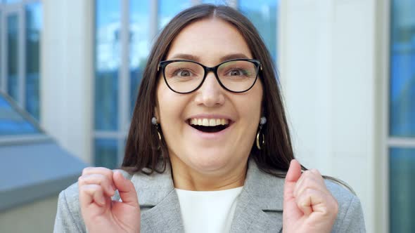 Closeup of a Young Woman in Glasses Smiling with Surprise at the Camera