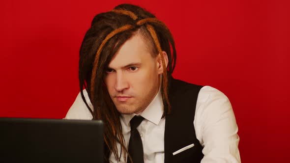 Young Conceptual Man in Business Suit Working at Laptop Red Background