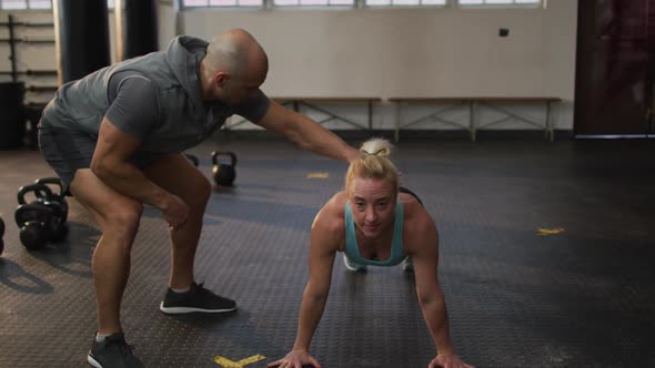 Male trainer correcting form of fit caucasian woman while push up exercise at the gym
