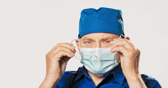 Mature Visually Impaired Doctor Puts on Protective Goggles Dressed in Blue Uniform with Bandana on