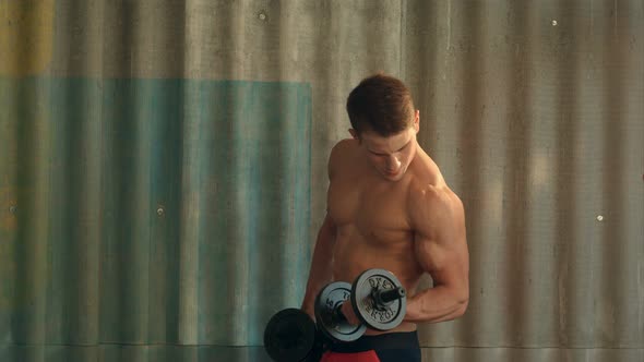 Torso Shot of a Young Man with Bare Chest Lifting Dumbbells