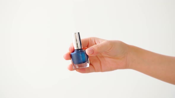 Female Hand Holding Nail Polish Bottle Against White Background