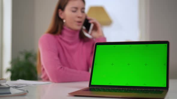 Green Screen of Laptop with Blurred Woman Talking on Phone at Background