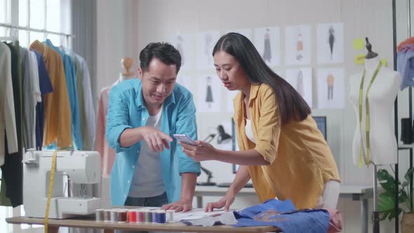 Asian Male And Female Designers Comparing Clothes Drawing Pictures To The Pictures On Smartphone