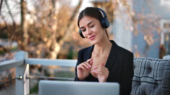 Joyful Woman in Headphones Talking Online Video Call Use Laptop on Balcony